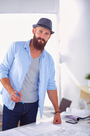 Portrait of male designer in hat with blueprints at deskの写真素材