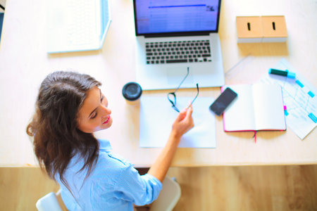 Young woman sitting in office table, looking at laptop computer screen . Young womanの写真素材
