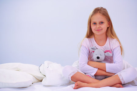 Little girl in the bedroom is sitting on the bed. Little girl is wearing a pajamas and sitting in bed .の写真素材