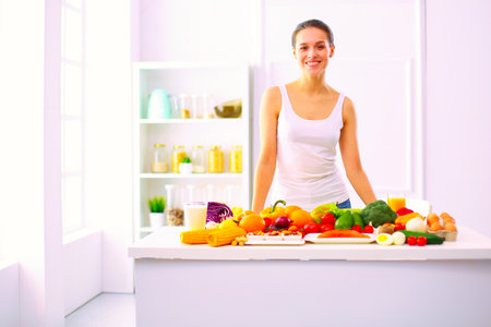 Young and cute woman sitting at the table full of fruits and vegetables in the wooden interiorの写真素材