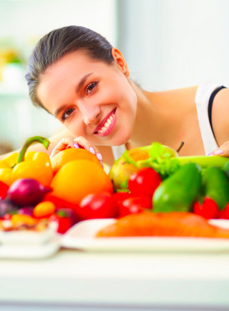 Young and cute woman sitting at the table full of fruits and vegetables in the wooden interiorの写真素材