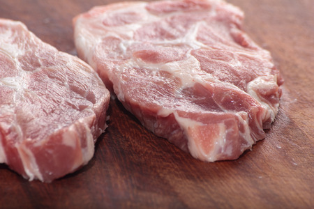 Two pieces of raw pork neck on a wooden board.の写真素材