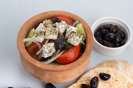 Greek salad in a clay pot with pitas and appetizers.の写真素材