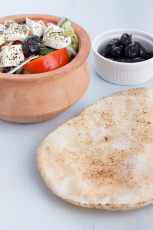 Greek salad in a clay pot with pitas and appetizers.の写真素材