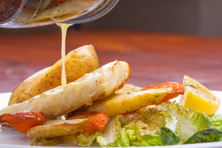 Cod fish with sauted vegetables and roman lettuce are being treated with white sauce.の写真素材