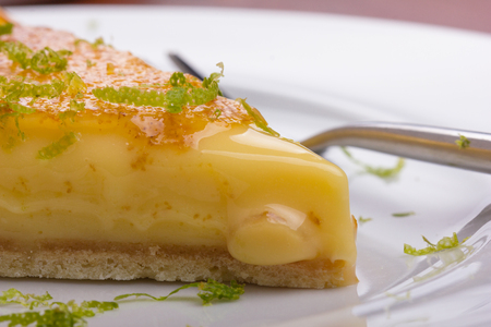 Lemon tart with lime zest served on a white plate.の写真素材