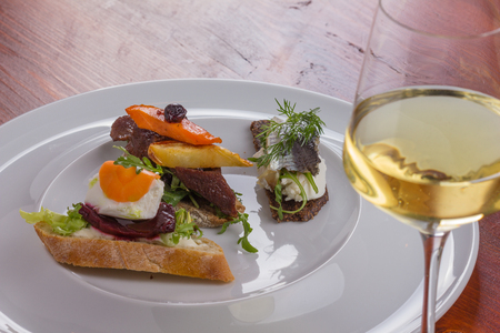 Glass of white wine and tartines with meat and veggies.の写真素材