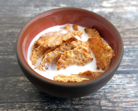 Wheat bran breakfast cereal with milk in clay bowl on wooden background