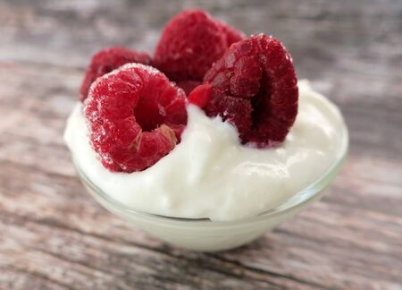 Freshly frozen raspberries with white yogurt in a glass cup on a wooden tableの写真素材