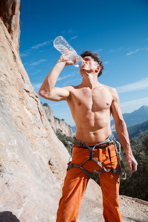 Handsome male rock climber drink water over the blue sky and mountains. Turkey, Geyikbayiri.の写真素材