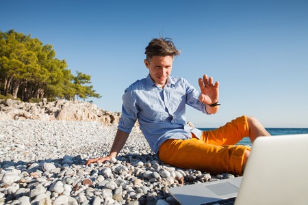 Handsome young barefooted man walking with laptop computer by the sea coastの写真素材