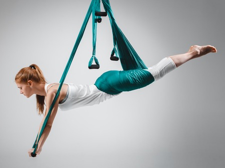 An adult woman practices different inversion - anti-gravity yoga positions in a bright well lit studio.の写真素材