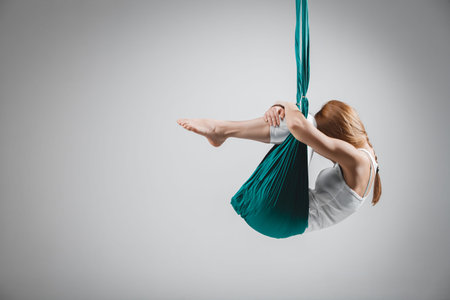 An adult woman practices different inversion - anti-gravity yoga positions in a bright well lit...