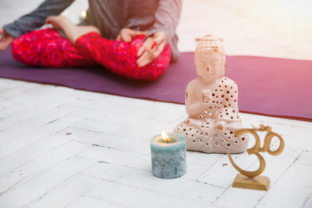 woman sitting in lotus asana and doing yoga meditation with spiritual accessories, candles and Buddha statueの写真素材