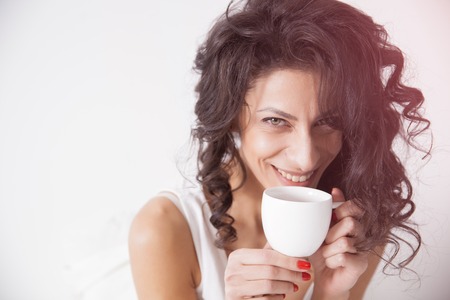 Closeup woman portrait with a cup of coffee on the bed under the duvet. Concept of happy family living, relaxation, home comfort, funの写真素材