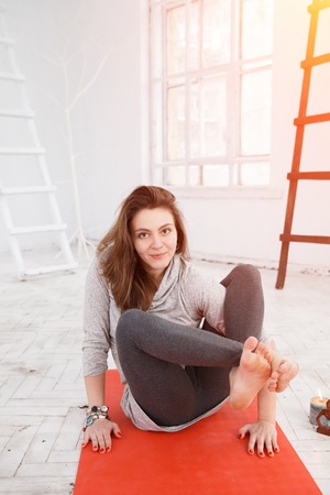 Handsome woman having yoga trainig on red gymnastic carpet in white lit room. Concept of physical and mental health, happy living and wellbeing.の写真素材