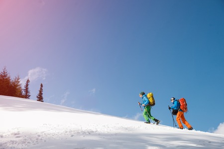 Two male hikers against blue sky in winter mountains passing away from camera. Concept of success living and free traveling, active leisure, health care and well being.の写真素材