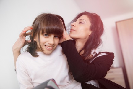 Young mother and daughter sitting on the sofa at home in white lit room against the window. Smooth morning light, casual style - concept of happy family living and lifestyleの写真素材