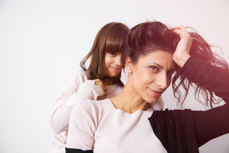 Young mother and daughter sitting on the sofa at home in white lit room against the window. Smooth morning light, casual style - concept of happy family living and lifestyleの写真素材