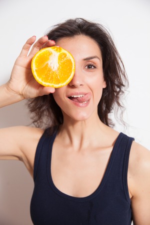 Portrait of young smiling woman cover her eye with orange. Concept of vegetarian dieting, raw food ingredients, healthy and joyful livingの写真素材