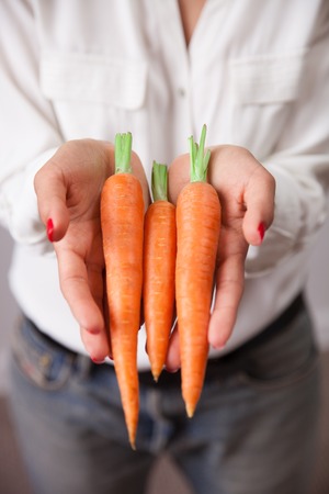 Young woman hands with carrot - closeup photo. Concept of vegetarian dieting, raw food ingredients, healthy and joyful livingの写真素材