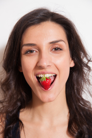 Young woman holding strawberry on lips - closeup portrait photo. Concept of vegetarian dieting, raw food ingredients, healthy and joyful livingの写真素材