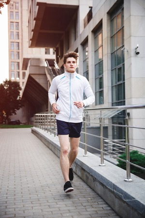 Adult male athlete running on downtown against office buildings . Concept of hard working and active living, freelance, remote business, healthcare and wellbeingの写真素材