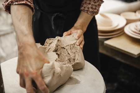 Adult male potter master preparing the clay on table. Front view, closeup, hands only. Art and business, hobby and freelance working concept.の写真素材
