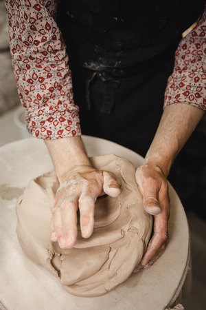 Adult male potter master mashing the clay on table. Front view, closeup, hands only. Art and business, hobby and freelance working concept.の写真素材