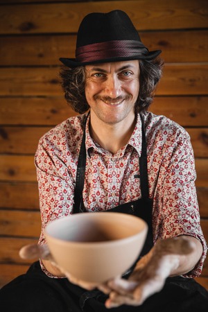 Adult male potter master creating new ceramic bowl on pottery wheel. Front view, closeup portrait. Art and business, hobby and freelance working concept.の写真素材