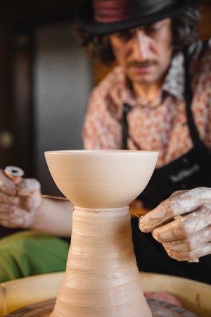 Adult male potter master creating new ceramic bowl on pottery wheel. Front view, closeup, focus on hands. Art and business, hobby and freelance working concept.の写真素材