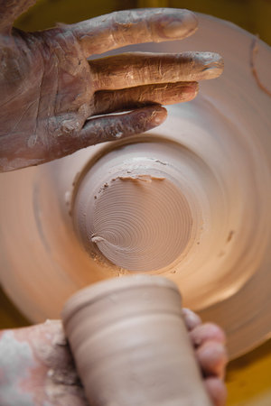 Adult male potter master creating new ceramic jug on pottery wheel. Top view, hands only closeup....