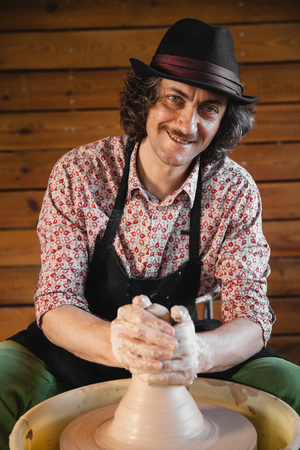 Adult male potter master creating new ceramic jug on pottery wheel. Front view, closeup portrait. Art and business, hobby and freelance working concept.の写真素材