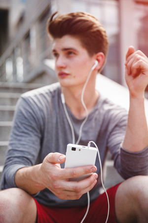 Athlete taking rest in city park with smartphone on stairs against office buildings before urban running. Concept of active living, freelance, remote business, healthcare and wellbeingの写真素材