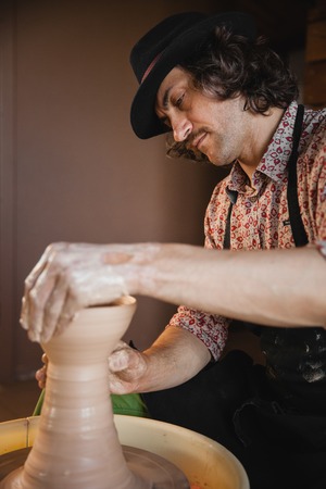 Adult male potter master creating new ceramic bowl on pottery wheel. Front view, closeup portrait. Art and business, hobby and freelance working concept.の写真素材