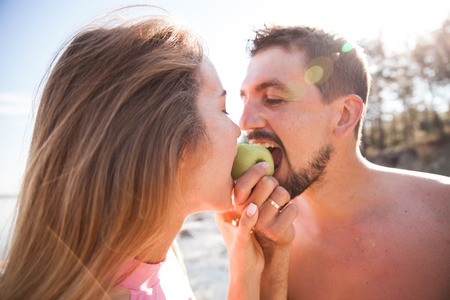 Young couple bitting green apple on the beach. Front view closeup - concept of harmony with the nature, free and healthy living, freelance, remote business.の写真素材