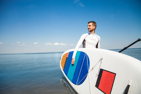 Young man with sup board and paddle on the beach - concept of harmony with the nature, free and...