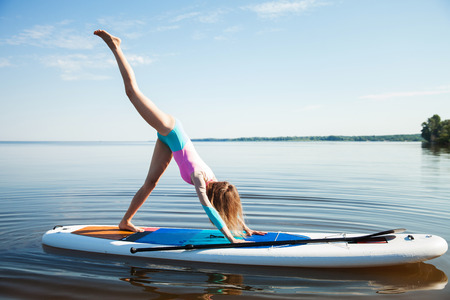 Young woman doing yoga on sup board with paddle. Mediatative pose, side view - concept of harmony with the nature, free and healthy living, freelance, remote business.の写真素材