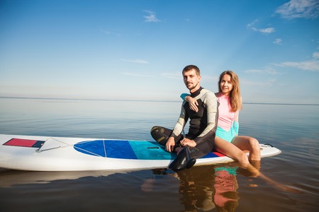 Young couple paddling on sup board with paddle. Sitting poses, side view - concept of harmony with the nature, free and healthy living, freelance, remote business.の写真素材
