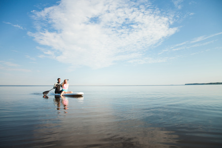 Young couple paddling on sup board with paddle. Sitting poses, side view - concept of harmony with the nature, free and healthy living, freelance, remote business.の写真素材
