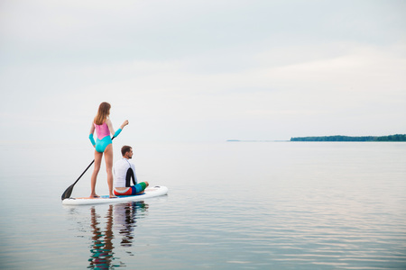 Young couple paddling on sup board with paddle, back view - concept of harmony with the nature, free and healthy living, freelance, remote business.の写真素材