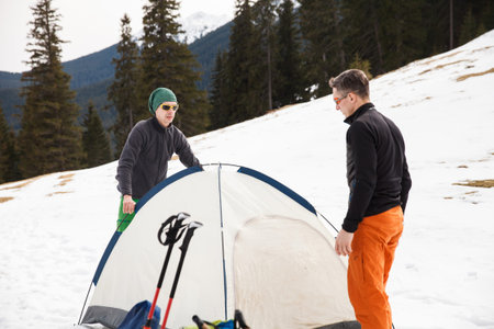 Two hikers in winter mountains installing tent. Concept of success living and free traveling, active...