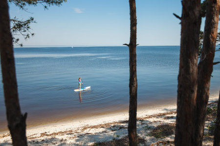 Unrecognizable young woman paddling on sup board with paddle. Sitting pose - concept of harmony with...