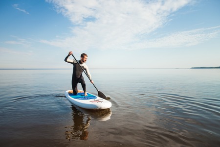 Young man paddling on sup board with paddle. Sitting pose - concept of harmony with the nature, free and healthy living, freelance, remote business.の写真素材