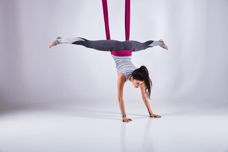 Young woman practices aerial different inversion anti-gravity yoga with a hammock in a white studio....