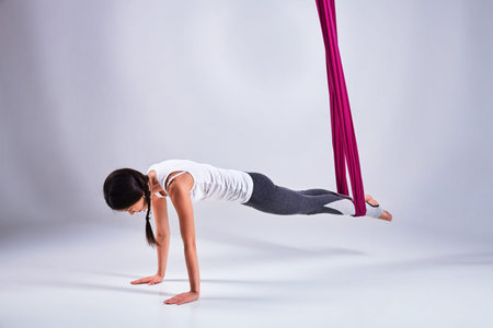 Young woman practices aerial different inversion anti-gravity yoga with a hammock in a white studio....