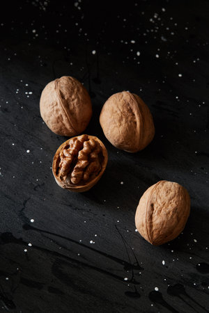 Close-up crop of walnuts and kernels on a black rustic backdrop. Healthy raw snack or organic...