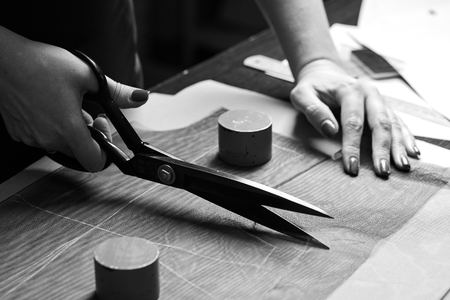 Cutting up the fabric with tailor scissors for further bespoke exclusive fashioning. Tailor atelier - handmade exclusive clothes making and repair, private business, creative occupation conceptの写真素材