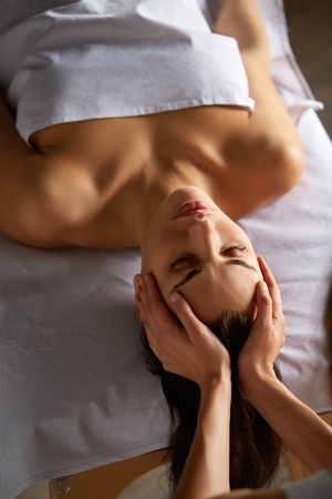 Close-up of female enjoying relaxing head and face massage made by masseuse with forearms and cubits in cosmetology spa centre. Body care, skin care, wellness, wellbeing, beauty treatment concept.の写真素材