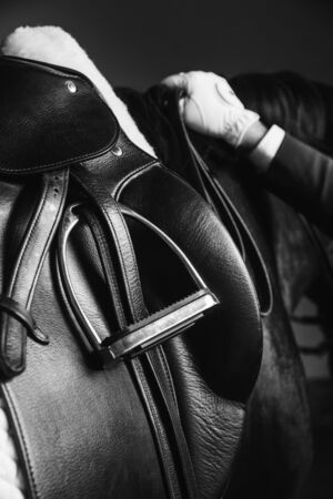 Jockey saddle up the thoroughbred horse for dressage or equestrian race. Stirrup, reins and hand on the mane. Noble aesthetics, dress code, professional equipment, competition and excitement conceptの写真素材